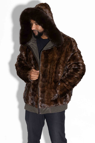 man wearing a brown reversible sheared sectioned mink fur bomber jacket with brown fox fur trimmed hood against a white backdrop