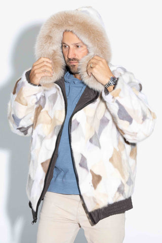 man wearing a reversible natural multicolor sectioned mink fur bomber jacket with brown fox fur trimmed hood against a white backdrop, with the hood up