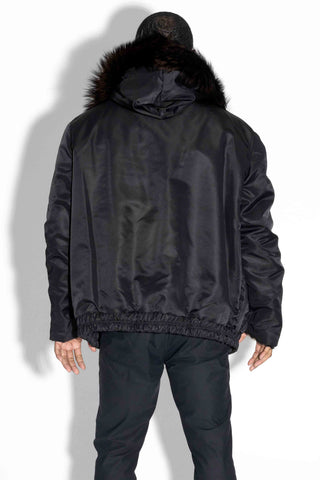 back of man wearing a ranch and brown reversible sectioned mink fur bomber jacket, with brown fox fur trimmed hood, and black cloth side facing out, against a white backdrop