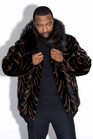 man wearing a ranch and brown multicolor reversible sectioned mink fur bomber jacket with black fox fur trimmed hood against a white backdrop