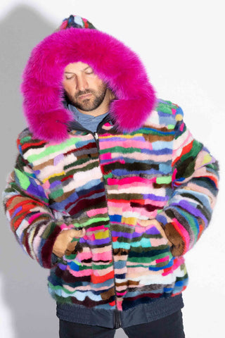 man wearing a pink multicolor sectioned mink fur jacket with pink fox fur trimmed hood up, against a white backdrop