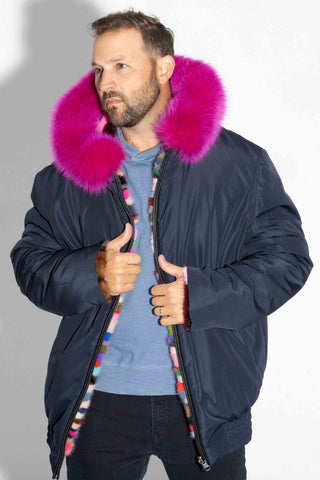 man wearing a pink multicolor sectioned mink fur bomber jacket with fox fur trimmed hood, and navy cloth lining facing out, against a white backdrop