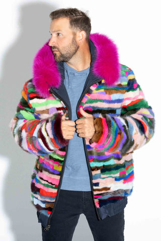 man wearing a pink multicolor reversible sectioned mink fur bomber jacket with pink fox fur trimmed hood against a white backdrop