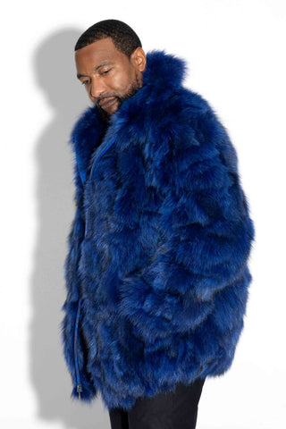 side profile of man wearing a blue sectioned fox fur bomber jacket against a white background, with his hands in pockets of jacket