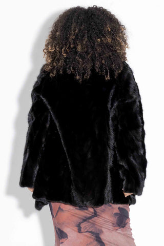 back of woman wearing a ranch sectioned mink fur jacket with notch collar and adjustable waist against a white backdrop