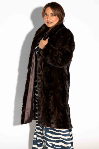 side profile of woman wearing a sheared sectioned mink fur 3/4 coat against a white backdrop