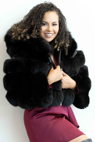 woman wearing a black fox fur jacket with horizontal pattern and hood against a white backdrop