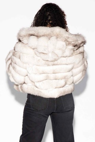 back of woman wearing a blue fox fur jacket with horizontal pattern and hood against a white backdrop