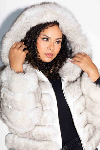 woman wearing a blue fox fur jacket with hood against a white backdrop