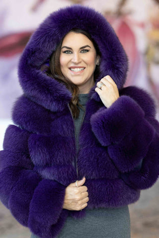 smiling woman wearing a purple fox fur jacket with horizontal pattern and hood