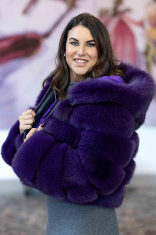side profile of woman wearing a purple fox fur jacket with horizontal pattern and hood, with black leather inserts