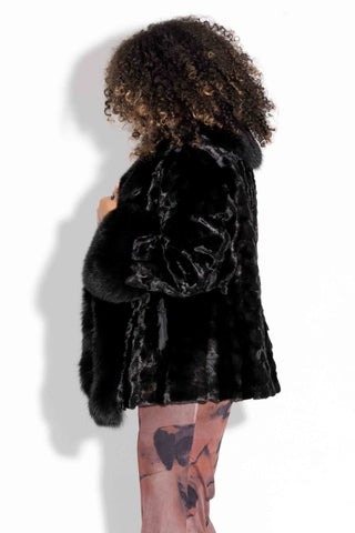 side profile of woman wearing a ranch sectioned mink fur jacket with black fox fur trim against a white backdrop