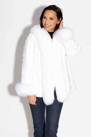 smiling woman wearing a white sheared sectioned mink fur jacket with white fox fur trim against a white backdrop