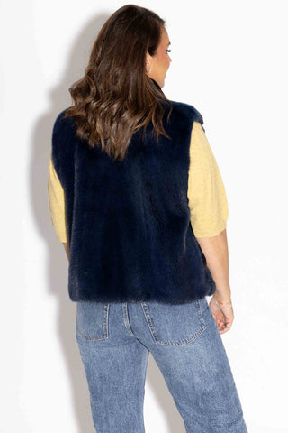 back of woman wearing a navy chinchilla fur vest with mink fur back against a white backdrop