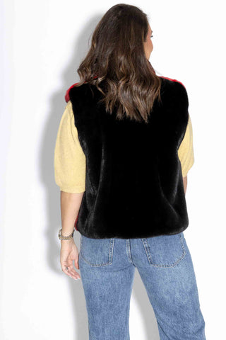 back of woman wearing a red chinchilla fur vest with ranch mink fur back against a white backdrop