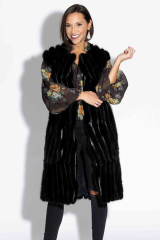 smiling woman wearing a long ranch chevron sectioned mink fur vest with leather inserts against a white backdrop