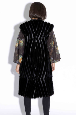 back of woman wearing a long ranch chevron sectioned mink fur vest with leather inserts against a white backdrop