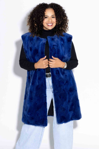smiling woman wearing a royal blue sectioned mink fur vest against a white backdrop