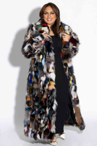 smiling woman wearing a full length multicolor sectioned fox fur coat against a white backdrop
