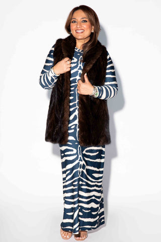 smiling woman wearing a mahogany chevron sectioned mink fur tails vest with shawl collar against a white backdrop