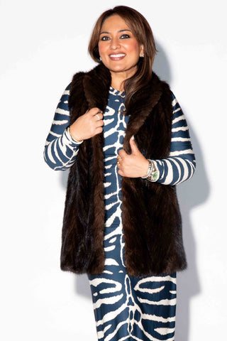 closeup of a smiling woman wearing a mahogany chevron sectioned mink fur tails vest with shawl collar against a white backdrop