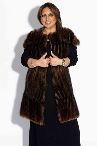 woman wearing a long chevron sectioned mink fur vest with cap sleeves and leather inserts against a white backdrop