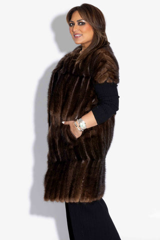 side profile of woman wearing a long mahogany chevron sectioned mink fur vest with cap sleeves against a white backdrop