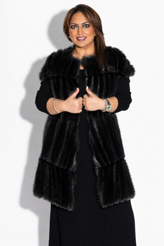 smiling woman wearing a long ranch chevron sectioned mink fur vest with cap sleeves and leather inserts against a white backdrop