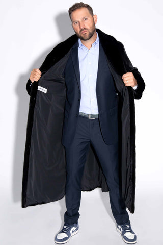 man wearing a blackglama ranch mink fur coat, showing off the blackglama tag, against a white backdrop