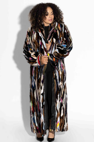 woman wearing a full length multicolor sectioned mink fur coat with shawl collar & bracelet cuffs against a white backdrop