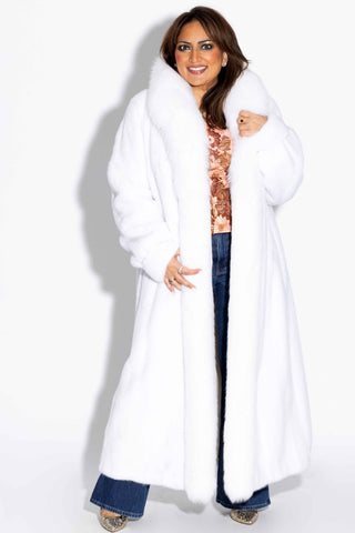 smiling woman wearing a white full length mink fur coat with fox fur tux against a white backdrop
