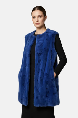 woman wearing a long blue sectioned mink fur vest against a white backdrop