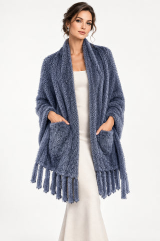 woman wearing a blue knitted mink fur shawl with fringe and pockets against a white backdrop