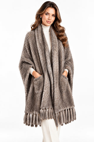 woman wearing a gray knitted mink fur shawl with fringe and pockets against a white backdrop