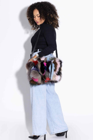 woman looking down at and wearing a multicolor fox fur purse with black against a white backdrop